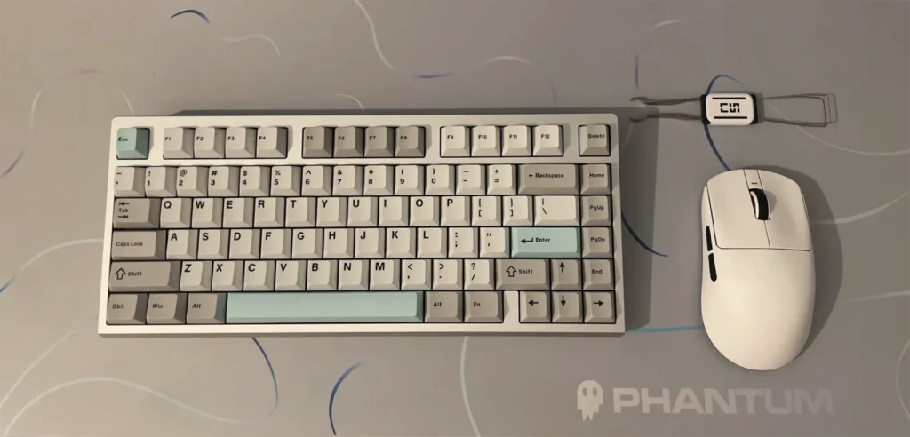 White and mint-accent mechanical keyboard and white mouse on a grey Phantum mousepad with abstract line art