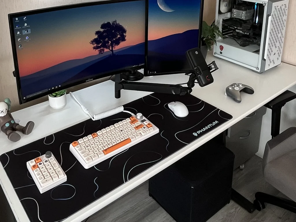 Photo prise sur le vif d’un bureau gamer à domicile avec tapis Nebula noir Phantum aux motifs blancs en boucle, clavier séparé et souris sous deux écrans